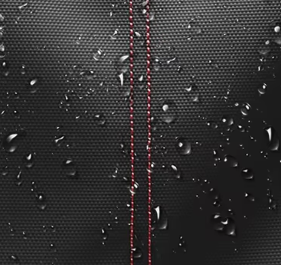 Close-up of waterproof black travel backpack fabric with red stitching and water droplets